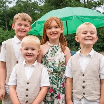 Four children smiling together under a green umbrella at an Oak Tree Farm wedding