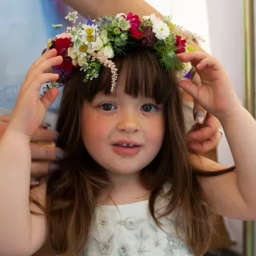 Young flower girl having a beautiful floral crown placed on her head at Oak Tree Farm wedding