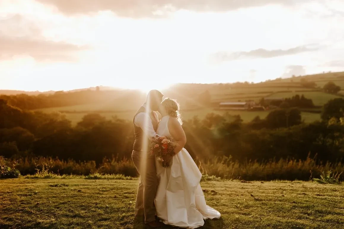 Bride and groom embracing at golden sunset with Welsh countryside rolling hills behind them