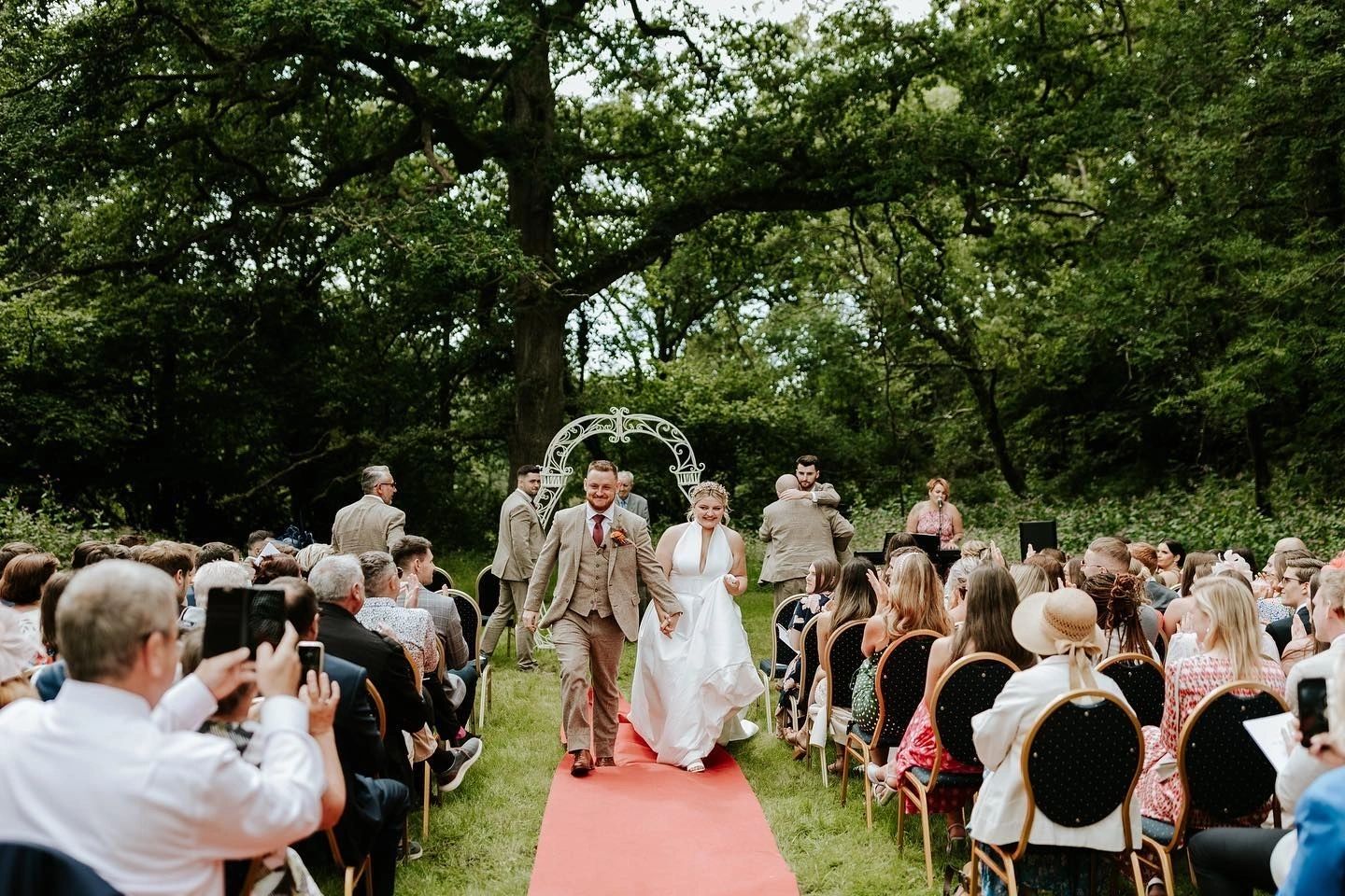 Outdoor wedding ceremony beneath a floral arch in a woodland garden